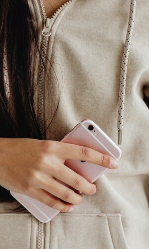 A woman in a beige hoodie holds a pink smartphone, showcasing casual style.