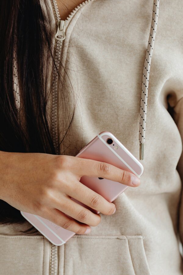 A woman in a beige hoodie holds a pink smartphone, showcasing casual style.